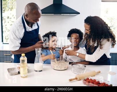 Glückliche afroamerikanische Familie, die zusammen in ihrer Küche backt. Fröhliche Mutter und Vater spielen beim Kochen mit ihren Söhnen. Brüder, die einen mischen Stockfoto