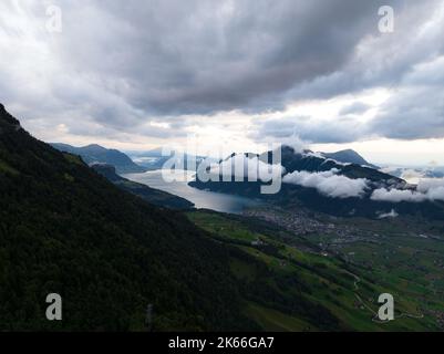 Schweizer Berg bei Sonnenuntergang Drohnenübersicht im Kanton Schwyz. Tief hängende Wolken über dem Bergsee bei Schwyz Zentralschweiz. Stockfoto