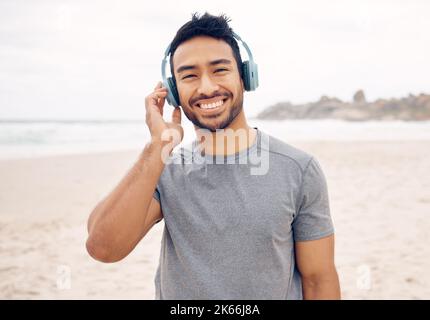 Ich fühle mich weniger gestresst, wenn ich im Freien bin. Porträt eines sportlichen jungen Mannes, der Kopfhörer trägt, während er am Strand trainiert. Stockfoto