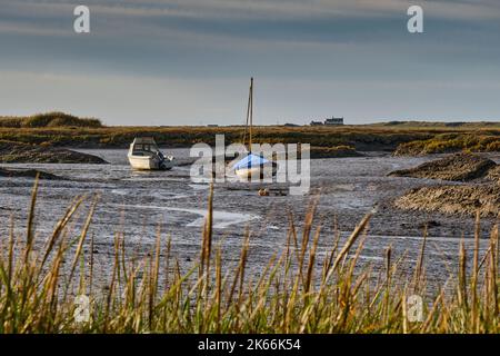 Boote bei Ebbe in Brancaster Staithe, mit dem Royal West Norfolk Golf Club Haus in Brancaster in der Ferne, Norfolk Stockfoto