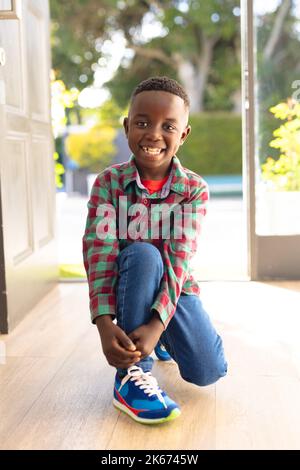 Vertikales Bild eines glücklichen afroamerikanischen Jungen, der jemanden außerhalb des Hauses begrüßt Stockfoto