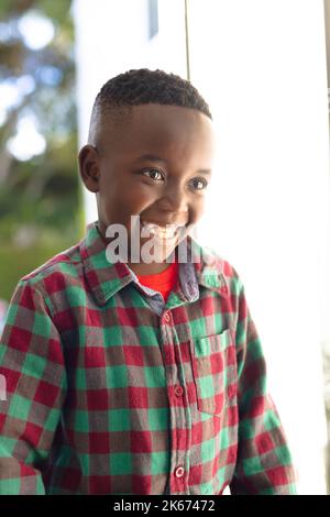 Vertikales Bild eines glücklichen afroamerikanischen Jungen, der jemanden außerhalb des Hauses begrüßt Stockfoto