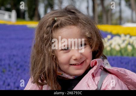 Lächelndes kleines Mädchen im Park, geschmückt mit bunten Tulpen. Selektiver Fokus Mädchen Gesicht Stockfoto