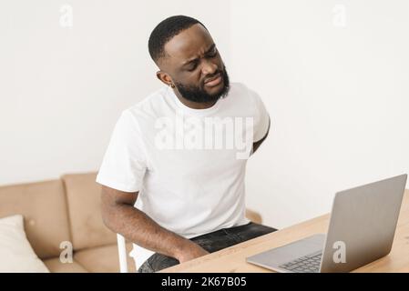 Junge erschöpfte afroamerikanische Arbeiterin hat Rückenbeschwerden aufgrund langer Arbeit am Schreibtisch im Home Office. Müde, zwanglose Geschäftsmänner-Atmosphäre Stockfoto