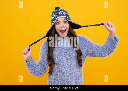 Schöne Winter Kinder Porträt. Teenager Mädchen posiert mit Winter Pullover und Strickmütze auf gelbem Hintergrund. Aufgeregt Teenager Mädchen. Stockfoto