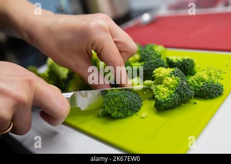 Frau schneidet Brokkoli mit einem Messer auf einem grünen Schneidebrett Stockfoto