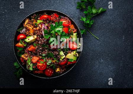 Quinoa Tabbouleh Salat mit Tomaten, Paprika, Avocado, Gurken, Zwiebeln und Petersilie. Traditionelles nahöstliches und arabisches Gericht. Schwarzer Küchentisch Stockfoto