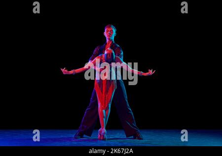 Zwei tanzende Personen, Tanztänzer in eleganten Outfits in Bewegung, Action auf dunklem Hintergrund in Neonlicht. Konzept von Kunst, Musik, Tanz, Emotionen. Stockfoto