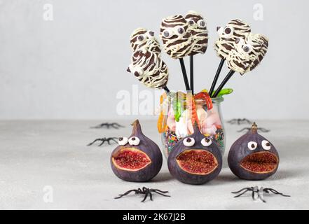 Gruselige Feigenmonster, Mama geformte Schokoladenkuchen-Pops und Gummiwürmer für Halloween-Party auf grauem Hintergrund Stockfoto