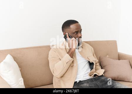 Seriöser schwarzer Freiberufler, der von zu Hause aus telefoniert. Junger afroamerikanischer Geschäftsmann, der mit Kunden über das Mobiltelefon spricht. Stockfoto