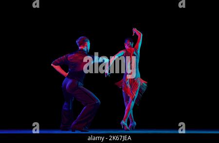 Zwei tanzende Personen, Tanztänzer in eleganten Outfits in Bewegung, Action auf dunklem Hintergrund in Neonlicht. Konzept von Kunst, Musik, Tanz, Emotionen. Stockfoto
