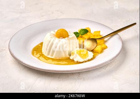 Löffel und Stück hausgemachte Panna Cotta mit natürlicher Vanilleschote, Mango-Sirup und Minze, selektiver Fokus Stockfoto