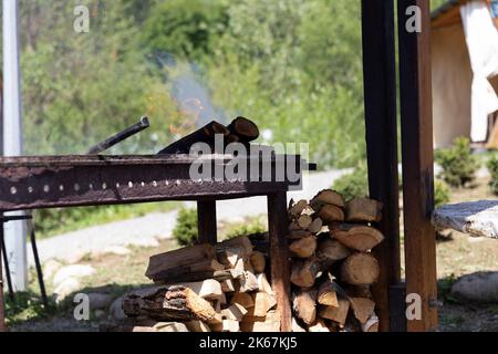 Alte Grill mit brennenden Holzstämmen. Offenes Feuer aus einem Metallkasten. Snack an der frischen Luft in einem Naturpark. Ein Ort zum Kochen von Fleisch und Gemüse Stockfoto