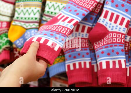 Weibliche Hand- und warme Socken mit farbenfrohem Muster auf einem Kleiderbügel. Frau, die Outfit und Geschenke für die Weihnachtsfeiertage wählt Stockfoto