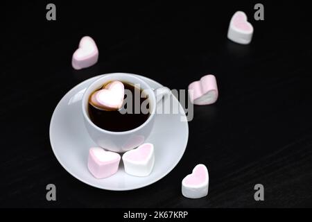 Weiße Tasse Kaffee oder Tee mit marsmalow Herzen auf dunklem Holztisch. Heißes Getränk mit Süßigkeiten, romantischer Morgen Stockfoto