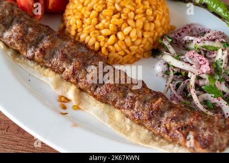 Adana Kebab auf Holzhintergrund. Traditionelle türkische Kebab-Delikatessen. Nahaufnahme Stockfoto