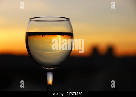 Weinglas mit Stadtgebäuden, die auf dem Hintergrund des Sonnenuntergangs reflektiert werden. Konzept der Feier, Weinindustrie Stockfoto