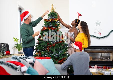 Bild von fröhlichen, vielfältigen Freunden, die zu Hause weihnachten feiern und den Baum schmücken Stockfoto
