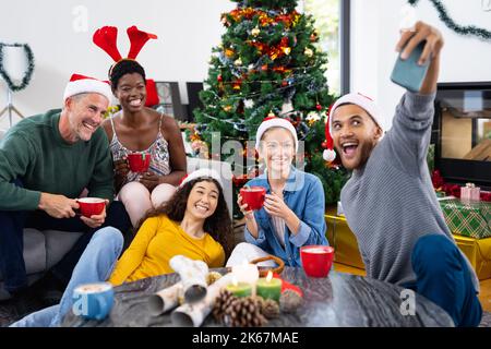 Bild von fröhlichen, vielfältigen Freunden, die zu Hause weihnachten feiern und Selfie machen Stockfoto