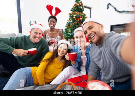 Bild von fröhlichen, vielfältigen Freunden, die zu Hause weihnachten feiern und Selfie machen Stockfoto