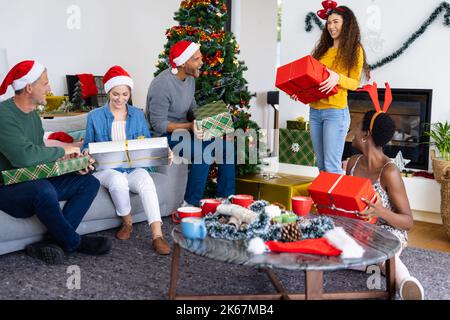 Bild von fröhlichen, vielfältigen Freunden, die zu Hause weihnachten feiern und Geschenke austauschen Stockfoto