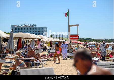 Ein Strandverkäufer läuft unter Sonnenanbetern und Strandbesuchern am Strand von Sottovento und versucht, Ketten zu verkaufen. In der Nähe von Gallipoli in Apulien (Apulien), Italien. Stockfoto