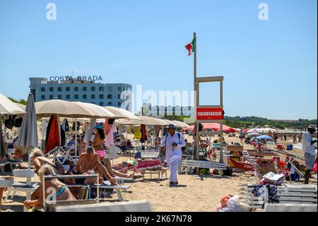 Ein Strandverkäufer läuft unter Sonnenanbetern und Strandbesuchern am Strand von Sottovento und versucht, Ketten zu verkaufen. In der Nähe von Gallipoli in Apulien (Apulien), Italien. Stockfoto