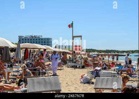 Ein Strandverkäufer läuft unter Sonnenanbetern und Strandbesuchern am Strand von Sottovento und versucht, Ketten zu verkaufen. In der Nähe von Gallipoli in Apulien (Apulien), Italien. Stockfoto