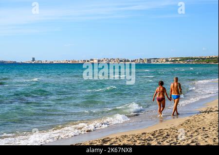 Blick über die Bucht nach Gallipoli vom Strand Sottovento mit einem älteren Paar, das auf dem Sand spazierend ist, Apulien (Apulien), Italien. Stockfoto