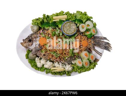 Köstlicher frittierter Fisch-Riesengurami und Kräutersalat mit knusprig gebratenem Knoblauch, serviert mit würziger Chilisauce auf grüner Keramik, isoliert auf wh Stockfoto