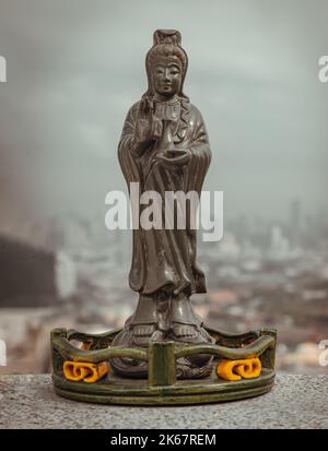 Figur der grünen Guan Yin Bodhisattva oder Quan Yin buddha Statue (Göttin der Barmherzigkeit) mit Blick auf die Stadt im Hintergrund. Platz für Text, selektiver Fokus. Stockfoto