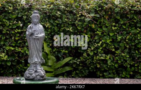 Figur der grünen Guan Yin Bodhisattva oder Quan Yin buddha Statue (Göttin der Barmherzigkeit) mit grünen Blättern Hintergrund. Platz für Text, selektiver Fokus. Stockfoto