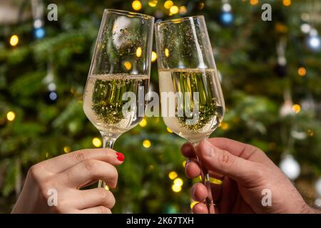 Man and woman clinking glasses with champagne against the Christmas tree. Celebrating the atmosphere of the New Year party.  Stockfoto