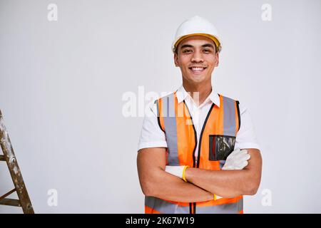 Porträt eines asiatischen Bauarbeiters, der lächelt, mit gekreuzten Armen, weißer Wand Stockfoto