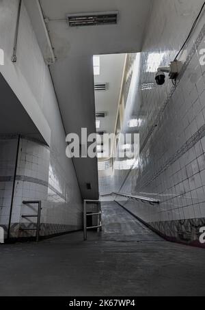 Bangkok, Thailand - Sep 30, 2022 : Treppen führen zur Innenansicht der öffentlichen Unterführung mit weiß gefliesten Wänden und CCTV. Raum für Text, selektiver Fokus Stockfoto