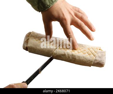 Die Hand eines Mannes mit einem Messer, das ein frisch zubereitetes Shawarma halbiert. Isoliert auf weißem Hintergrund. Stockfoto