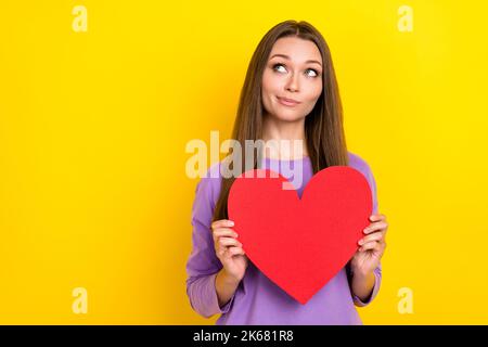 Foto von attraktiven niedlichen mädchenhaften Frau halten verträumt großen roten Papier Herz Pouted Lippen lächelnd suchen leeren Raum minded Datum App auf gelb isoliert Stockfoto