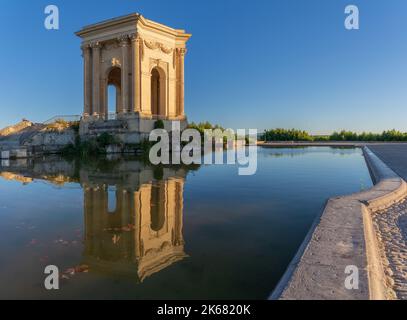 Blick auf den alten Wasserturm mit Spiegelung im Wasserbecken an einem Sommermorgen mit blauem Himmel im historischen Garten der Promenade du Peyrou in Montpellier, Frankreich Stockfoto