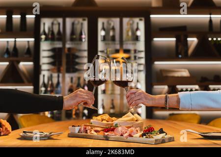 Ein romantisches Paar, das sich gegenüber am Esstisch im Weinzimmer saß, anklirrende Gläser und einen Weißwein schlürfte Stockfoto