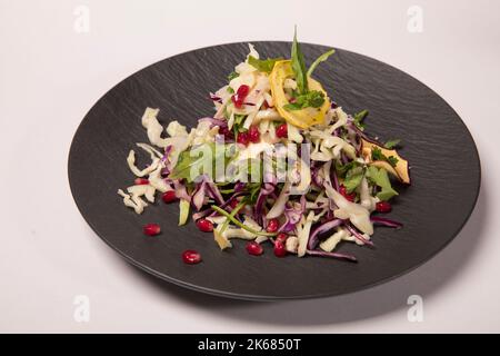 Eine Nahaufnahme von hausgemachtem Krautsalat aus frischem Kohl auf schwarzem Teller auf weißer Oberfläche Stockfoto