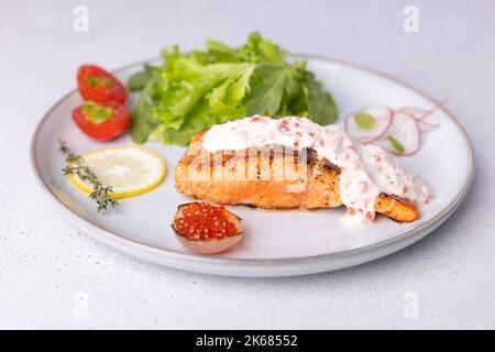 Lachs (Forelle) mit cremiger Champagnersauce mit rotem Kaviar, Rucola, Kirschtomaten, Rettich und Zitrone. Traditionelles französisches Gericht. Selektiver Fokus, clos Stockfoto