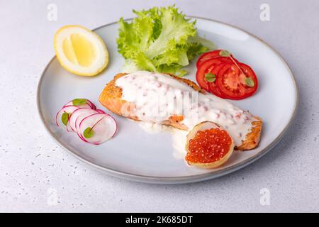 Lachs (Forelle) mit cremiger Champagnersauce mit rotem Kaviar, Salat, Tomaten, Rettich und Zitrone. Traditionelles französisches Gericht. Selektiver Fokus, Nahaufnahme. Stockfoto