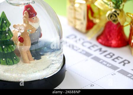 Weihnachtskonzept, Nahaufnahme der festlichen Schneekugel im Dezember-Kalender, Weihnachtsgeschenk und Glockenschmuck im Hintergrund Stockfoto