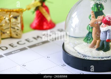 Weihnachtszeitkonzept, Nahaufnahme der festlichen Schneekugel im Dezember-Kalender, Weihnachtsgeschenk und Glocke im Hintergrund, selektiver Fokus Stockfoto