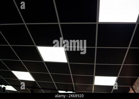 Schwarze Decke mit Neon-Glühbirnen in Aufstandsansicht. Fluoreszierendes Licht im Büroinnenraum mit dunkler Decke. Stockfoto