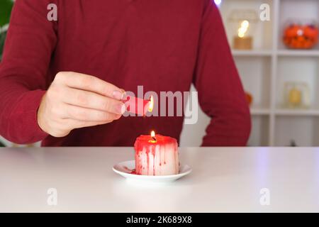 DIY Halloween Halloween weiße Kerze, bedeckt mit rotem Wachs wie Bluttropfen auf weißem Hintergrund. Geschenkidee, Dekor Halloween. Schritt für Schritt. Blutige Kerzen für Halloween-Urlaub. Workshop. Stockfoto