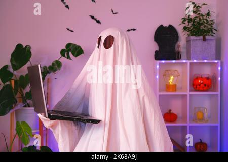 Der Geist von Halloween verwendet einen Laptop, um im Internet zu surfen, um Online-Shops, Märkte zu durchsuchen. Ein Geist macht einen Bestellcomputer für Halloween. Der Geist zahlt für einen Online-Kauf. Neonlicht. Stockfoto