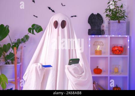 ghost Halloween verwendet Mobiltelefone, um im Internet zu surfen, in Online-Geschäften und auf Märkten zu stöbern. Der Geist macht eine Bestellung vom Smartphone für Halloween. Ghost bezahlt den Online-Kauf per Kreditkarte. Neonlicht. Stockfoto