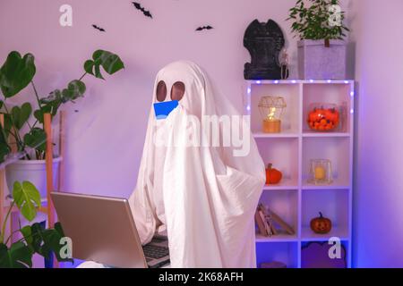 ghost of Halloween nutzt Laptop im Internet surfen, Online-Shops durchsuchen, Märkte. Ein Geist macht eine Bestellung vom Computer für Halloween. Ghost zahlt für den Online-Kauf per Kreditkarte. Neonlicht. Stockfoto