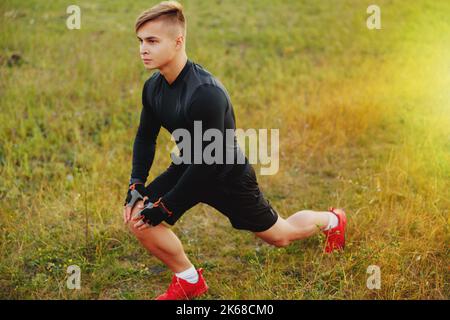 Junger Sportmann macht Dehnübungen vor dem Laufen oder Training im Freien auf Sonneneinstrahlung Hintergrund. Stockfoto